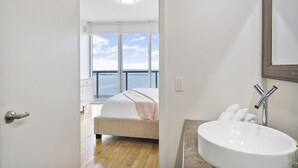 Une chambre avec une grande fenêtre, un lit, une salle de bain avec un lavabo et une vue sur la mer.