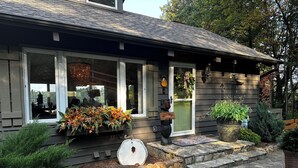 Una casa con un portico in pietra, un cartello di benvenuto e una vetrina decorata con foglie autunnali.