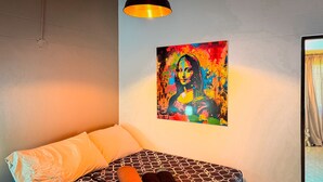 Un dormitorio con una cama, un cuadro de colores en la pared y una lámpara colgante.