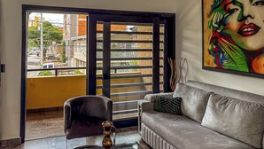 A living room with a sofa, a chair, a coffee table, and a large window with a view of buildings and a street. - Urban Loft Laureles : Modern, Elegant : A/C : Balcony (Medellín)
