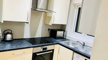 A compact kitchen with a stove, oven, microwave, sink, and a washing machine.
