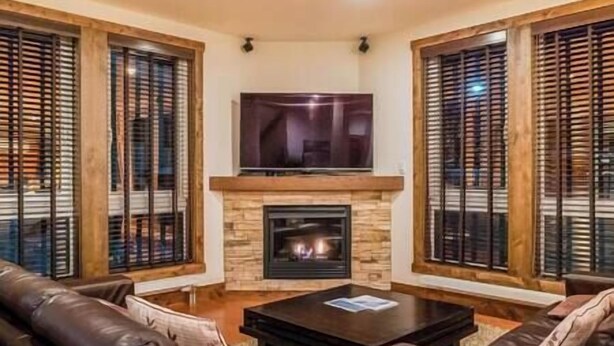 A living room with a fireplace, leather sofas, a TV, and wooden blinds. - Gouka Chalet by Elite Havens (Kutchan)