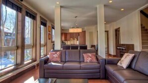 A spacious living room with a dark leather sofa, a coffee table, and large windows offering a view of the outdoors. - Gouka Chalet by Elite Havens (Kutchan)