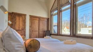 A bedroom with a large bed, wooden headboard, and a view of a house through the window. - Gouka Chalet by Elite Havens (Kutchan)