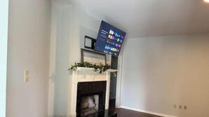 Un salon avec une cheminée, un téléviseur à écran plat fixé au-dessus, et un plaid jaune sur un canapé.