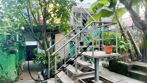 Una escalera con barandillas metálicas que conduce a un edificio, rodeado de follaje y plantas en macetas.