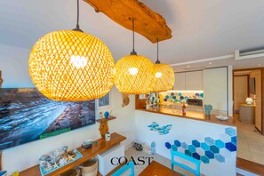 Une cuisine moderne avec un plan de travail en bois, un coin repas avec une chaise bleue et un grand téléviseur fixé au mur qui diffuse une vue panoramique.