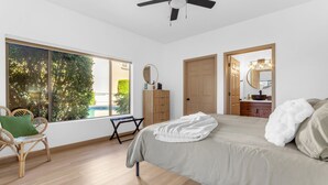 A bedroom with a large window, a bed, a chair, a ceiling fan, and a wooden door. - Cozy Condo in Beautiful Fountain Hills (Fountain Hills)