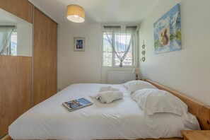 A neatly made bed with white linens, a book, and a painting on the wall.