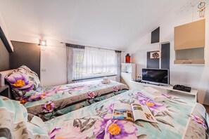 Ein Schlafzimmer mit zwei Betten, einem Fernseher, einem Bücherregal und einem Fenster mit Vorhängen.