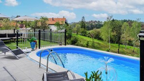 En swimmingpool med solstolar och ett staket, omgiven av grönska och hus.