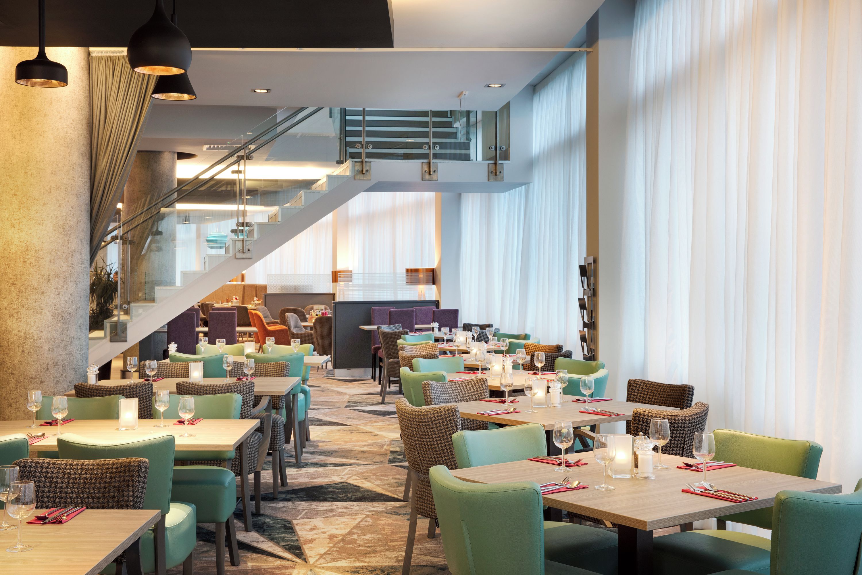 A modern restaurant with multiple dining areas, a staircase, and large windows.