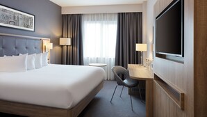 Habitación de hotel con una cama grande, un escritorio, una silla, un televisor y una ventana con cortinas.