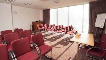Un salón de conferencias con sillas rojas, una mesa de madera, una pizarra y un reloj en la pared.
