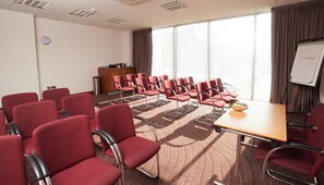 A conference room with red chairs, a wooden table, a whiteboard, and a clock on the wall. - Leonardo Hotel London Watford (Watford)