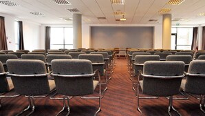 Un salón de conferencias con filas de sillas grises, una pantalla de proyección grande y suelo alfombrado.