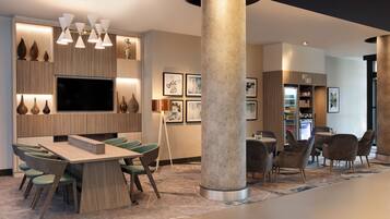 Un moderno hall de hotel con zona de comedor, un pilar grande y un refrigerador con aperitivos.