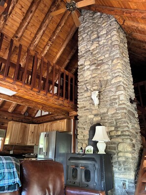 A rustic interior with exposed wooden beams, a stone fireplace with a cow skull, and a vintage stove.