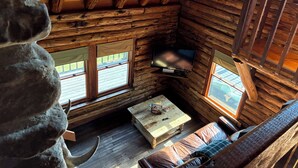 A rustic cabin interior with a wooden ceiling, a television mounted on the wall, a sofa, and a coffee table. - Chalet-Style Log Home  – Waynesville, Ohio (Waynesville)