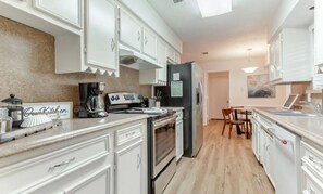 Una cocina moderna con armarios blancos, horno empotrado, refrigerador y cafetera.