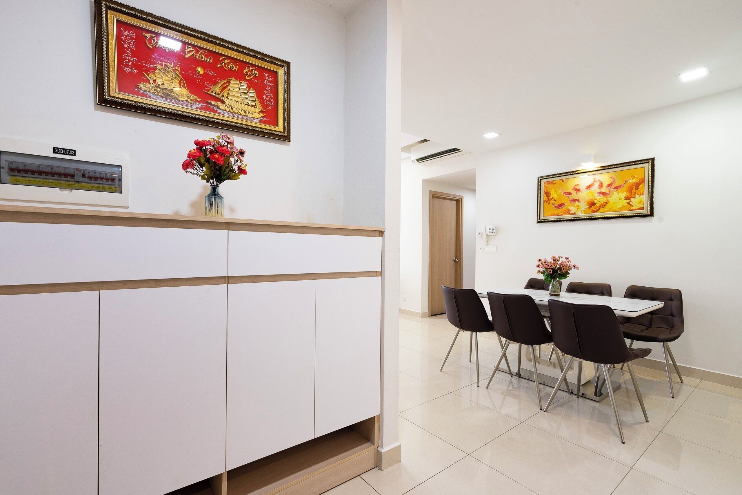 A hotel reception area with a reception desk, a telephone, a wall-mounted air conditioning unit, and a dining area with a table and chairs.