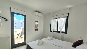 Ein Schlafzimmer mit Bett, zwei Kissen, einem Fenster mit Vorhängen, einer Klimaanlage und einer Tür zu einem Außenbereich mit Stuhl und Tisch.