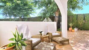 Eine Terrasse mit Korbmöbeln, einem Glastisch und Dekoration sowie mit Topfpflanzen.