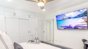 A bedroom with a bed, pillows, a ceiling fan, a TV, and a tray with bottles. - Ala Wishes Luxury Condo (Sosúa)