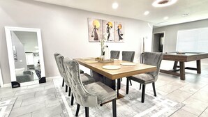 A dining area with a wooden table, grey upholstered chairs, and a modern ceiling light fixture. - NRG Stadium - Pool table, Patio, & Grill (Houston)