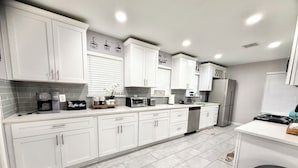 A modern kitchen with white cabinets, a coffee maker, a toaster, and a refrigerator. - NRG Stadium - Pool table, Patio, & Grill (Houston)