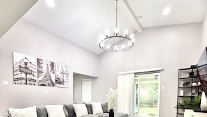 A modern living room with a sectional sofa, a wooden coffee table, and a chandelier. - NRG Stadium - Pool table, Patio, & Grill (Houston)