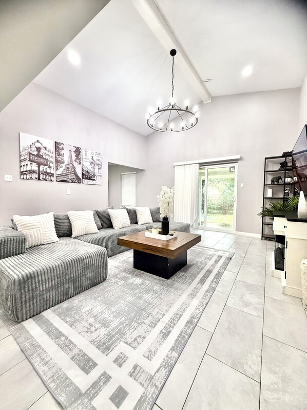 A modern living room with a sectional sofa, a wooden coffee table, and a chandelier. - NRG Stadium - Pool table, Patio, & Grill (Houston)