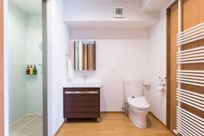 Um banheiro pequeno com vaso sanitário, pia e espelho. Há um porta-toalhas na parede e uma pequena prateleira com produtos de higiene pessoal.