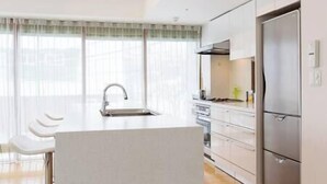 Una cocina moderna con una isla central, electrodomésticos de acero inoxidable y un amplio ventanal con cortinas translúcidas.