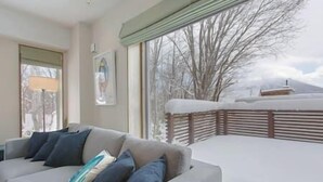 Una sala de estar con un sofá gris, una ventana con vistas a un paisaje nevado y un cuadro en la pared.