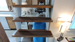 Una cocina con estantes de madera, un cubo de basura azul y una encimera blanca con una lámpara.