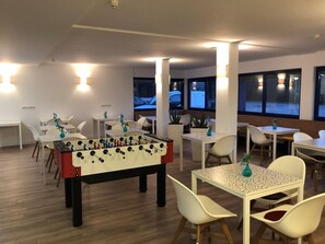 A room with multiple tables and chairs, a foosball table, and large windows with views of the outside.