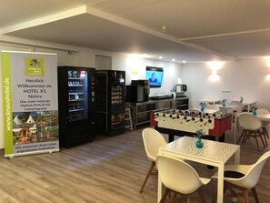 A hotel lobby with a foosball table, vending machines, a television, and a table with chairs. - Hotel K1 (Grammetal)