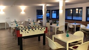Una stanza con diversi tavoli e sedie, un tavolo da calcio e ampie finestre che danno sull'esterno.