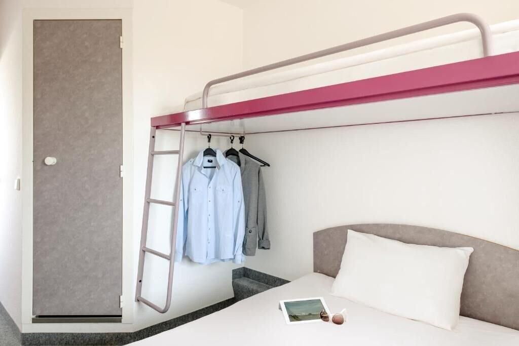 A bunk bed with a ladder, a bedside table with a book and sunglasses, and a clothing rack with hangers.