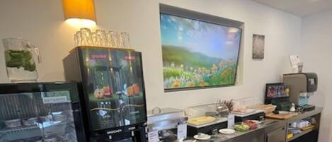 A modern kitchen area with a coffee machine, a glass display case with food items, and a large window with a view of greenery.