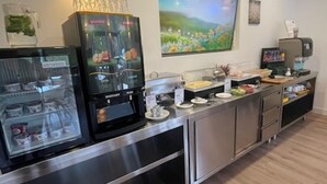 Un'area cucina moderna con una macchina da caffè, una vetrina in vetro con generi alimentari e un'ampia finestra vista verde.