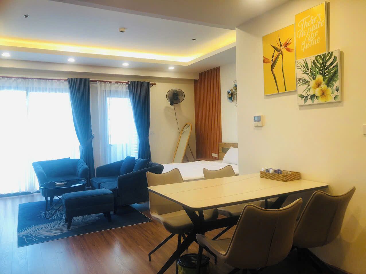 Una habitación de hotel moderna con comedor, un conjunto de sofás, un ventilador y obras de arte en las paredes.