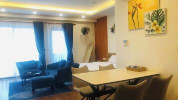 Una habitación de hotel moderna con comedor, un conjunto de sofás, un ventilador y obras de arte en las paredes.