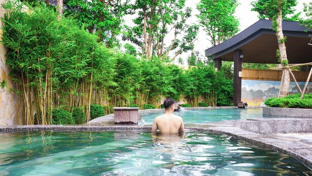 A man in a pool with clear water, surrounded by lush greenery and a covered pavilion. - FLC Sea Tower Quy Nhon Apartment (Quy Nhon Nam)