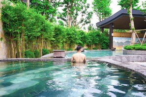 A man in a pool with clear water, surrounded by lush greenery and a covered pavilion. - FLC Sea Tower Quy Nhon Apartment (Quy Nhon Nam)