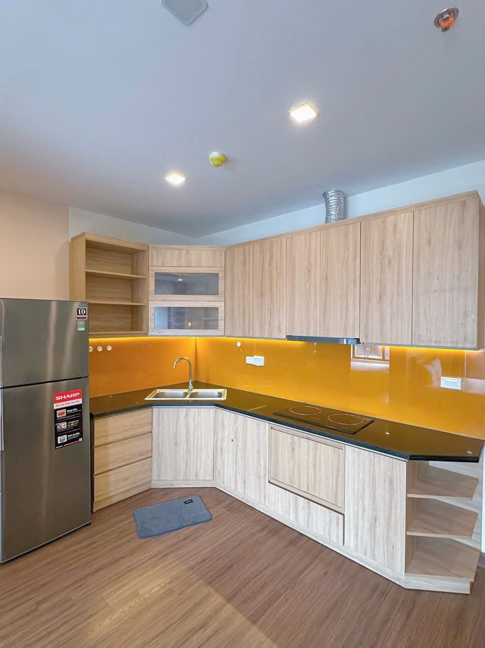 Une cuisine moderne avec des meubles en bois, un réfrigérateur en acier inoxydable et un plan de travail noir.
