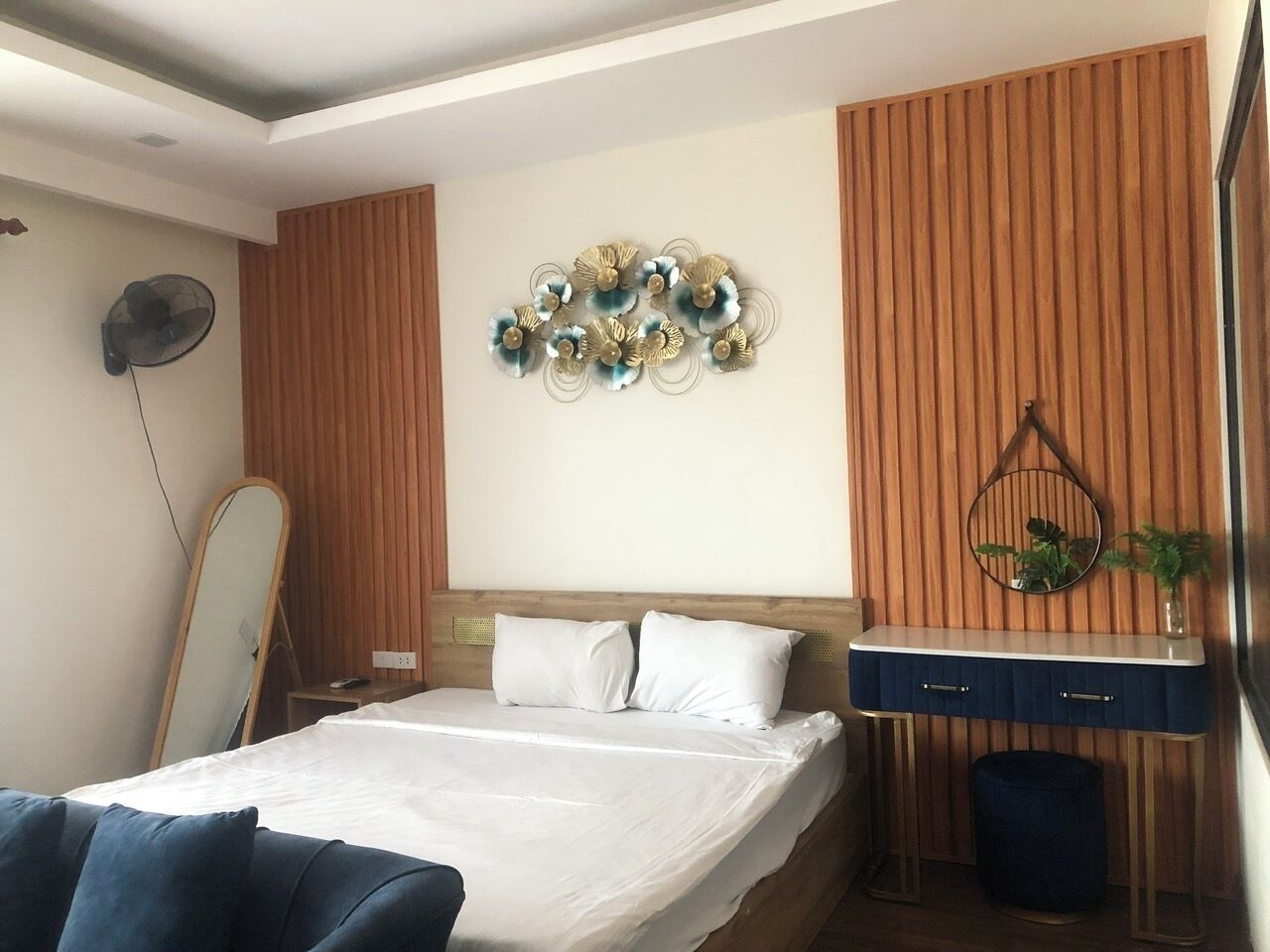 A bedroom with a bed, a bedside table, a mirror, and a wall decoration.