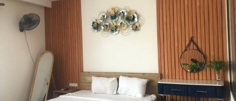 A bedroom with a bed, a bedside table, a mirror, and a wall decoration.
