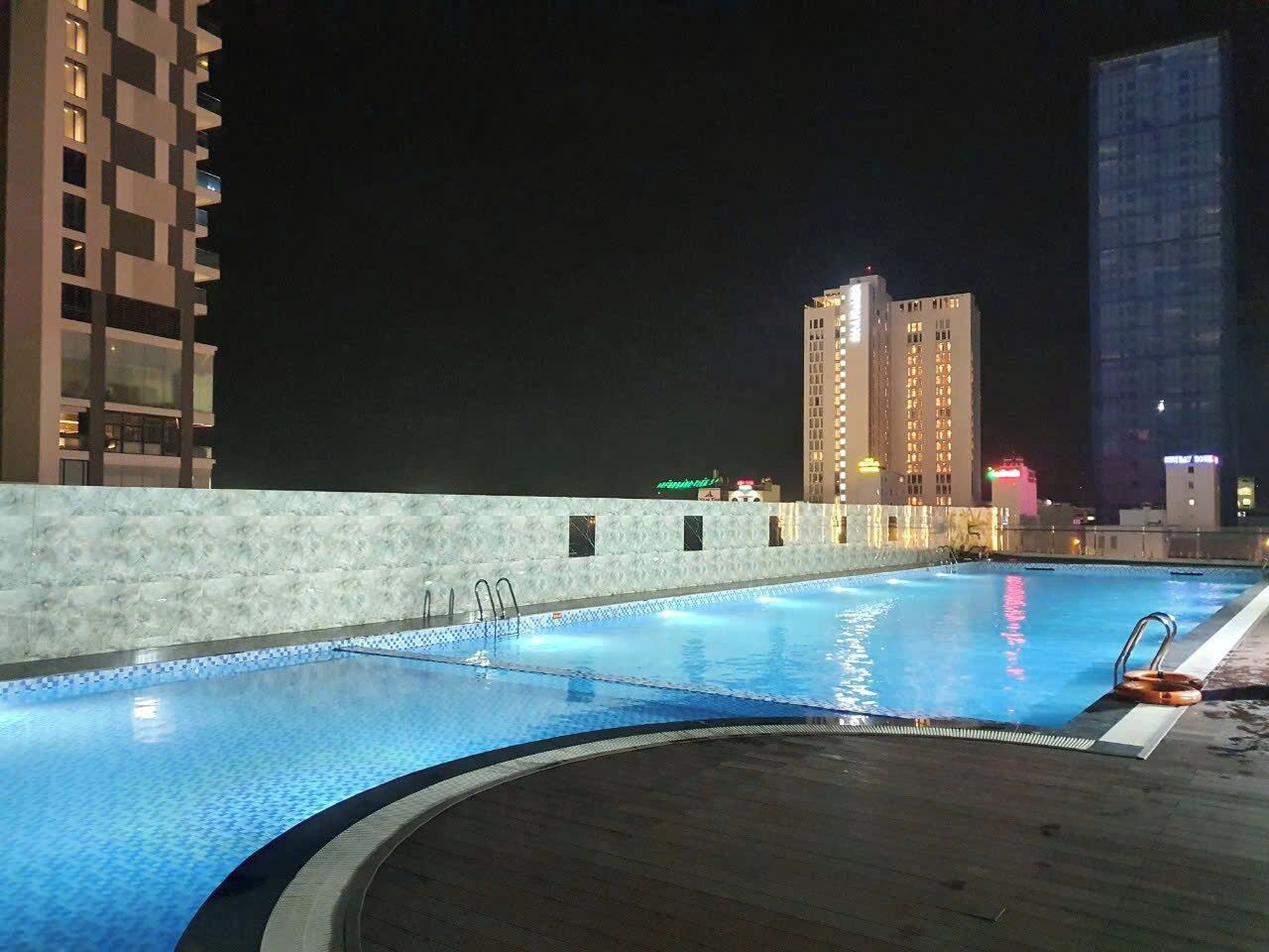 A rooftop swimming pool with a view of surrounding buildings at night.